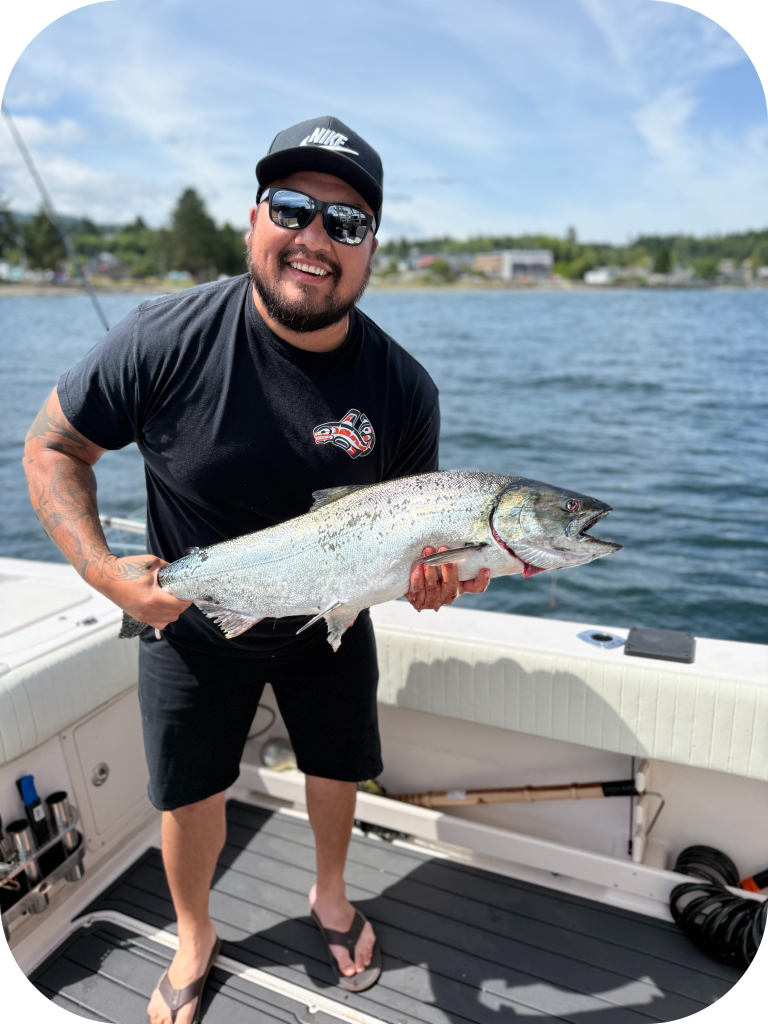 Man smiling and wearing glasses dressed in black holding large fish on a boat on open waters